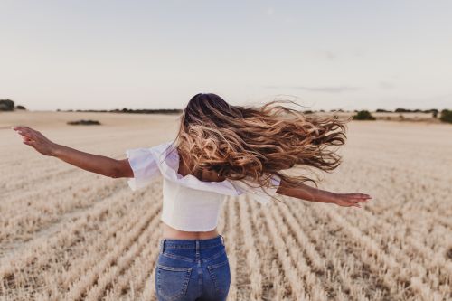 Frau auf einem Feld deren Haare durch den Wind fliegen
