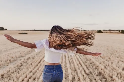 Frau auf einem Feld deren Haare durch den Wind fliegen