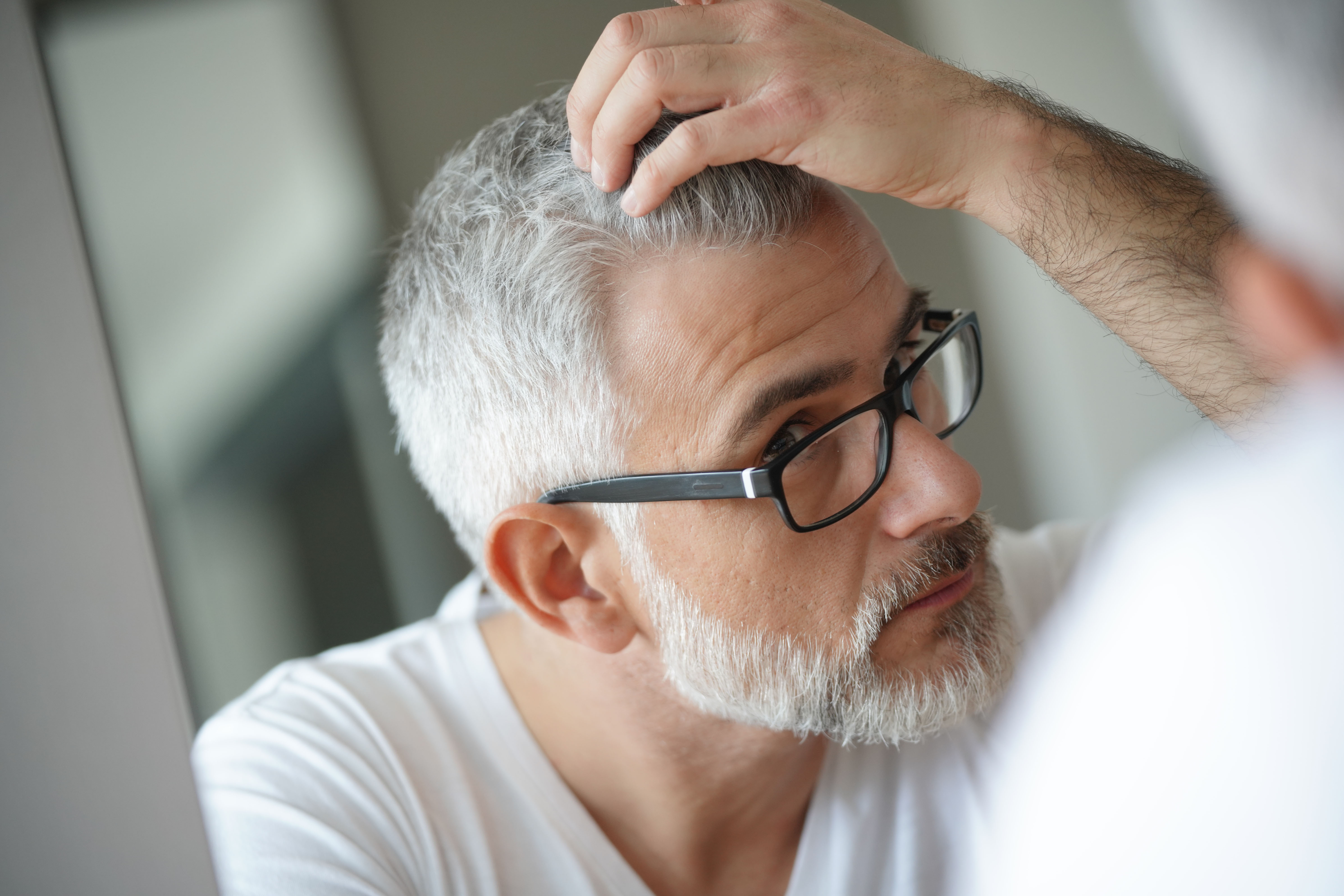 Mann mit Brille betrachtet seine Haare