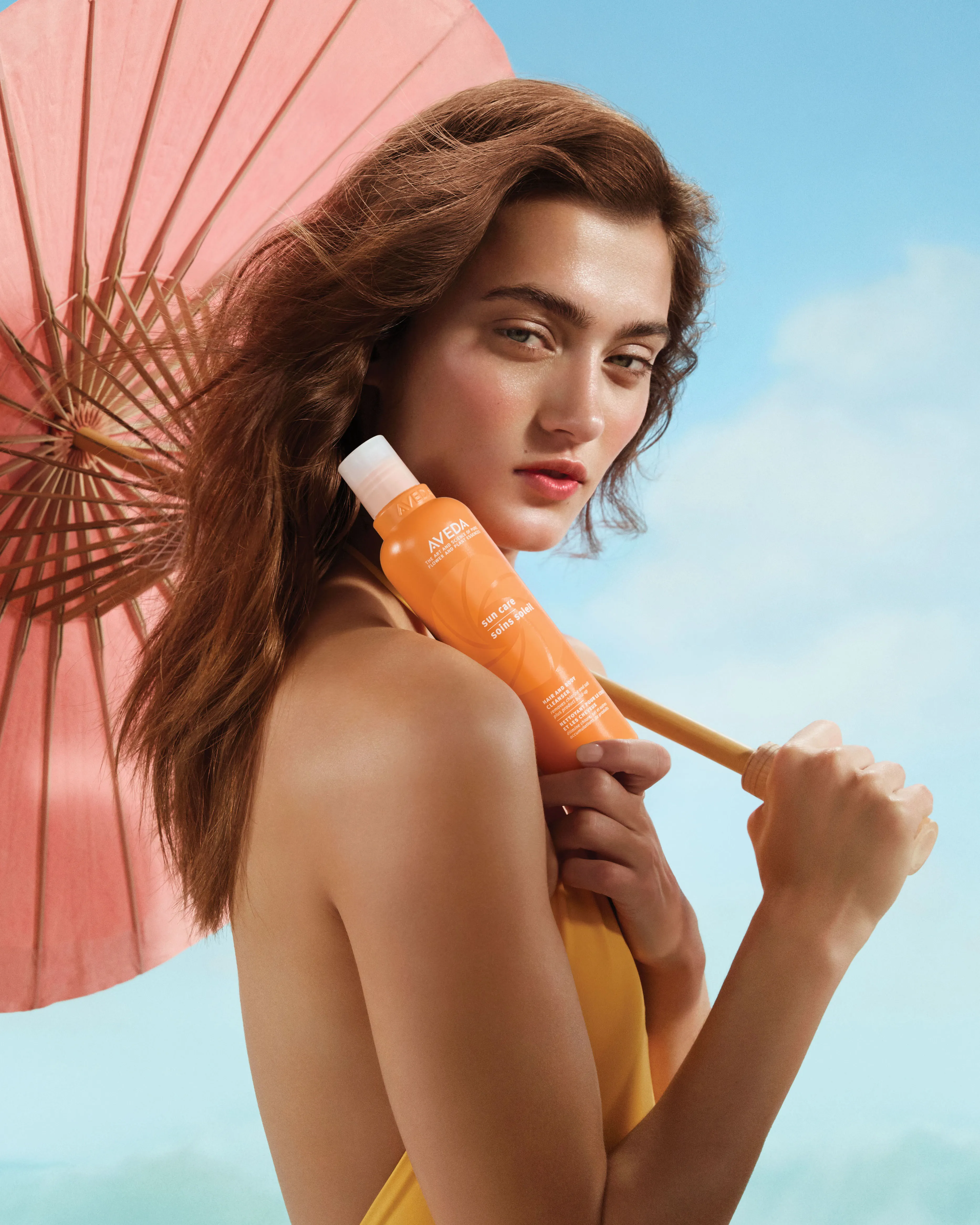 Frau mit Sonnenschirm hält Aveda Sun Care Protective Hair Veil in der Hand